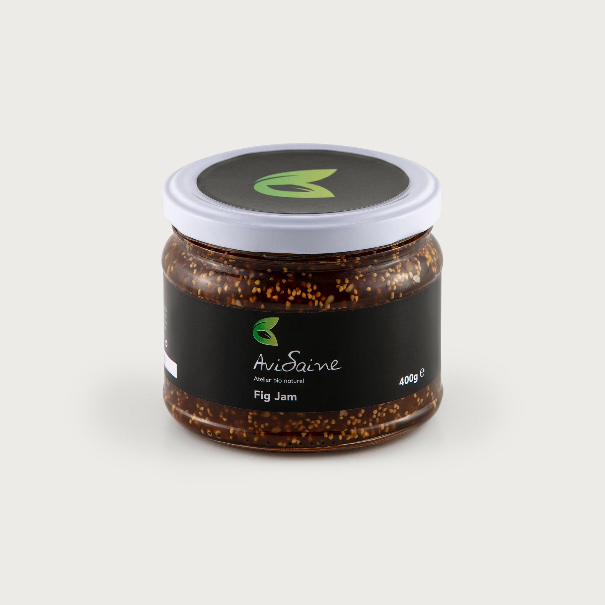 This clear 14 oz. jar of fig jam is rich brown in color with light brown fig seeds visible. The label is black with the green AviSaine logo, simple and modern.
