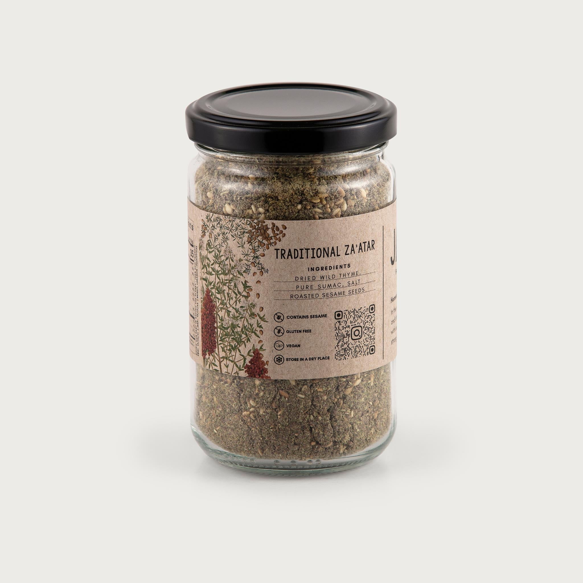 This clear jar of Traditional Za'atar showcases the beautiful ingredients inside. You can see the herbs, beautifully sage green, brown, and dried. The label is kraft brown in color and features illustrations of the herbs inside. The label reads: Traditional Za'atar with ingredients dried wild thyme, pure sumac, salt, roasted sesame seeds. Contains sesame, gluten free, vegan, and store in a dry place. There is a QR code on the front.